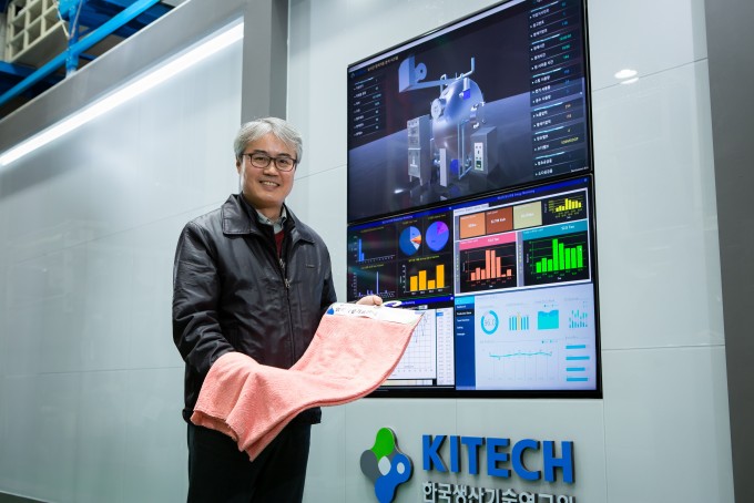 심재윤 한국생산기술연구원 스마트섬유그룹장 연구팀은 염색 상황을 실시간으로 파악해 불량 발생을 줄이는 ‘염색정보 실시간 통합 모니터링 기술’을 개발했다. 심 그룹장이 염색 정보가 표시된 모니터 앞에서 염색된 옷감을 들어 보이고 있다. 한국생산기술연구원 제공